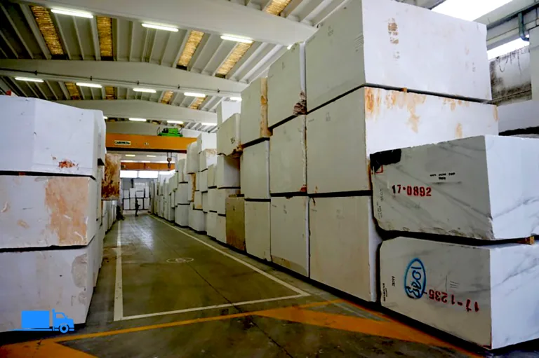 Magazyn z ułożonymi białymi blokami marmurowymi, gotowe do transportu